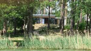 Une maison moderne entourée de grands arbres et bordée par un plan d’eau.