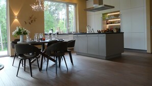Une cuisine moderne avec un coin repas, de grandes fenêtres et un lustre.