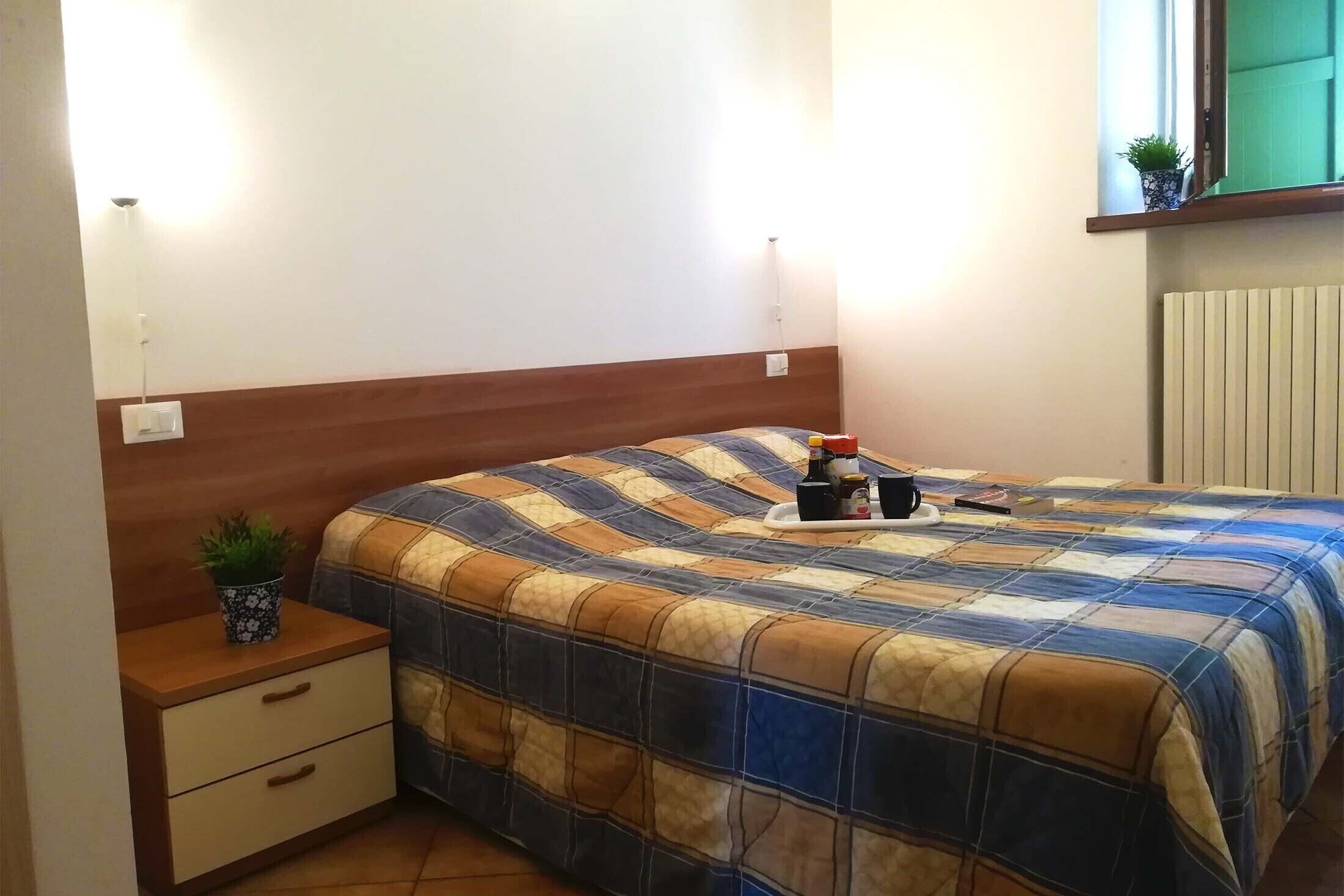 Une chambre à coucher avec une tête de lit en bois, une couvre-lit matelassé, une table de chevet ornée d’une plante et une fenêtre donnant sur un beau paysage.