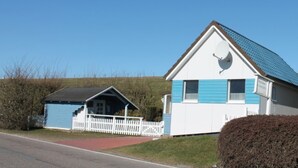 Ein zweigeschossiges Haus mit blauer und weißer Fassade, einer Satellitenschüssel auf dem Dach und einem kleinen Gartenhaus mit weißem Zaun.