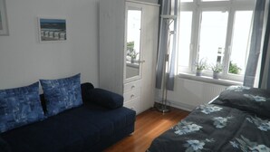A bedroom with a dark blue sofa, a bed with a floral bedspread, a wardrobe, and a window with a view of the outdoors. - Exclusive apartment (3 rooms, 85 sqm) in a quiet location, only 50m to the beach! (Heringsdorf)