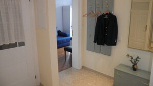 A hallway with a door, a coat rack with hangers, a small cabinet with a plant, and a glimpse of a room with a bed and a blue sofa. - Exclusive apartment (3 rooms, 85 sqm) in a quiet location, only 50m to the beach! (Heringsdorf)