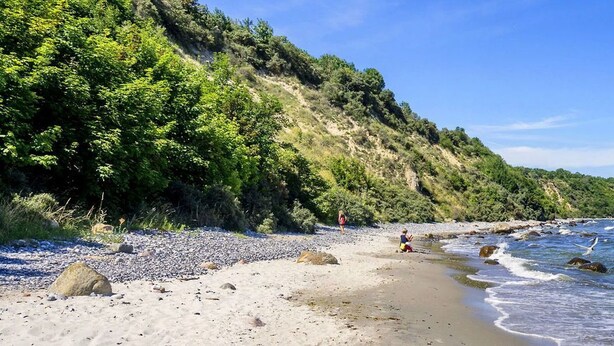 A beach with pebbles, a cliff, and the ocean.