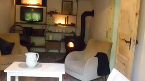 A cozy living room with a white sofa, a coffee table, and a television. There is a fireplace and a door to the right.