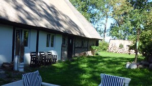 A thatched-roof building with outdoor seating and a stone wall in the background.