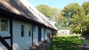 A traditional building with a thatched roof, a well-maintained lawn, and a stone wall in the background.