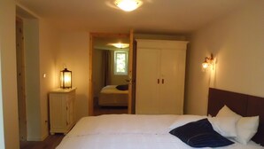 A bedroom with a large bed, a nightstand with a lamp, a wardrobe, and a window with curtains.