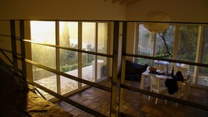 A spacious room with large windows, a dining area, and a staircase.