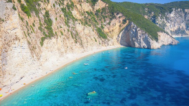 A coastal beach with clear turquoise waters, a sandy shoreline, and rocky cliffs.