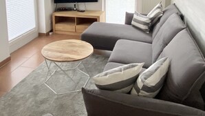 A modern living room with a grey sectional sofa, a wooden coffee table, a flat-screen TV on a wooden stand, and a grey rug.