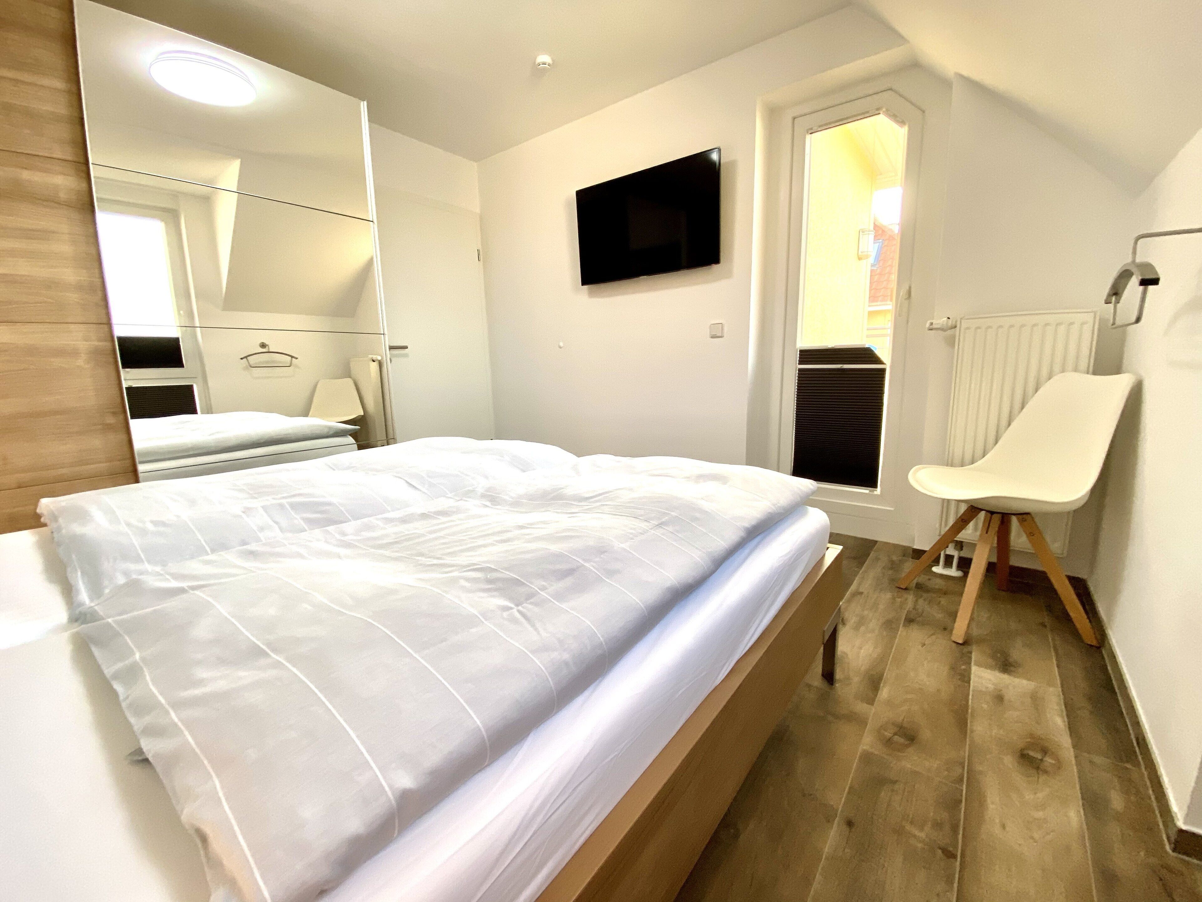 A bedroom with a bed, a chair, a TV, and a door.