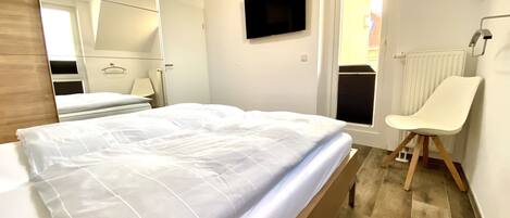 A bedroom with a bed, a chair, a TV, and a door.