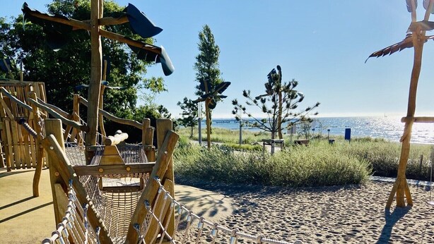 A wooden rope bridge over a sandy beach with a clear view of the ocean and trees in the background.