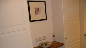Ein Flur mit einer weißen Tür, einem gerahmten Bild an der Wand, einem hölzernen Regal mit einer Schüssel und einem Glas sowie einer Steckdose.