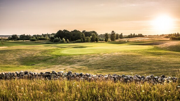 Een golfbaan met een stenen muur op de voorgrond en bomen in de verte.