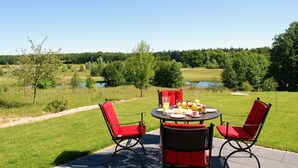 Een terras met een tafel en stoelen, met uitzicht op een golfbaan en een waterpartij op de achtergrond.