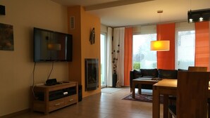 Een woonkamer met een televisie, open haard, bank en eettafel.