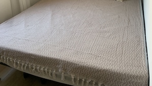 Un letto ben rifatto con copriletto decorato, due cuscini e un arazzo in macramè.