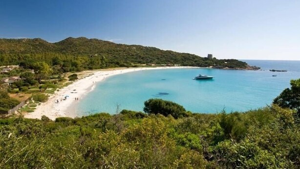Paesaggio costiero con spiaggia sabbiosa, acque blu cristalline e una barca.