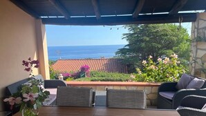 Una terrazza esterna con mobili in vimini, un tavolo in legno e vista sull'oceano.