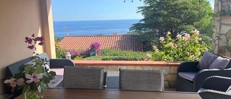 An outdoor patio with wicker furniture, a wooden table, and a view of the ocean.