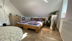 A bedroom with a loft bed, a bedside table, a chair, a radiator, and a window with a plant.