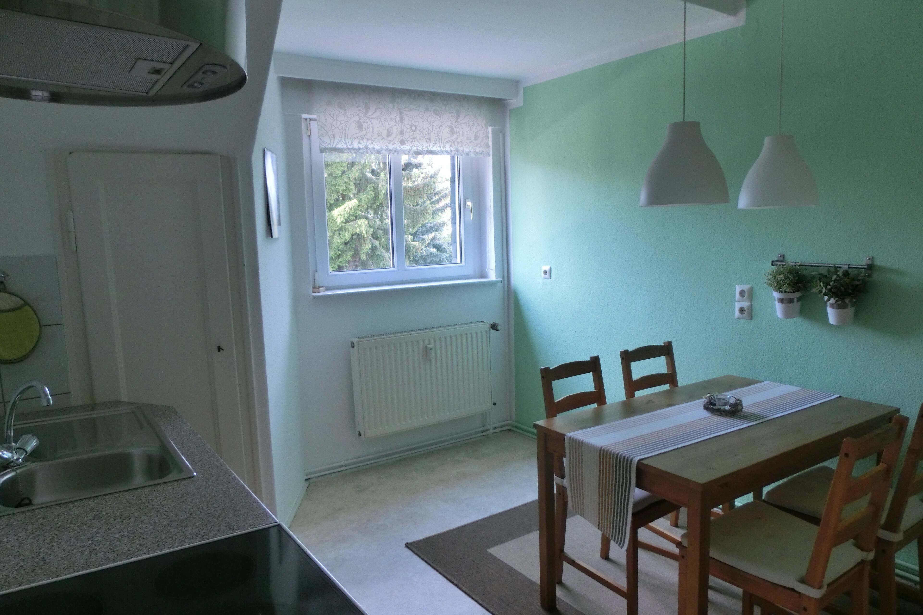 Eine Küche mit Fenster, Heizkörper, Spüle und einem Essbereich mit Stühlen und Tisch.