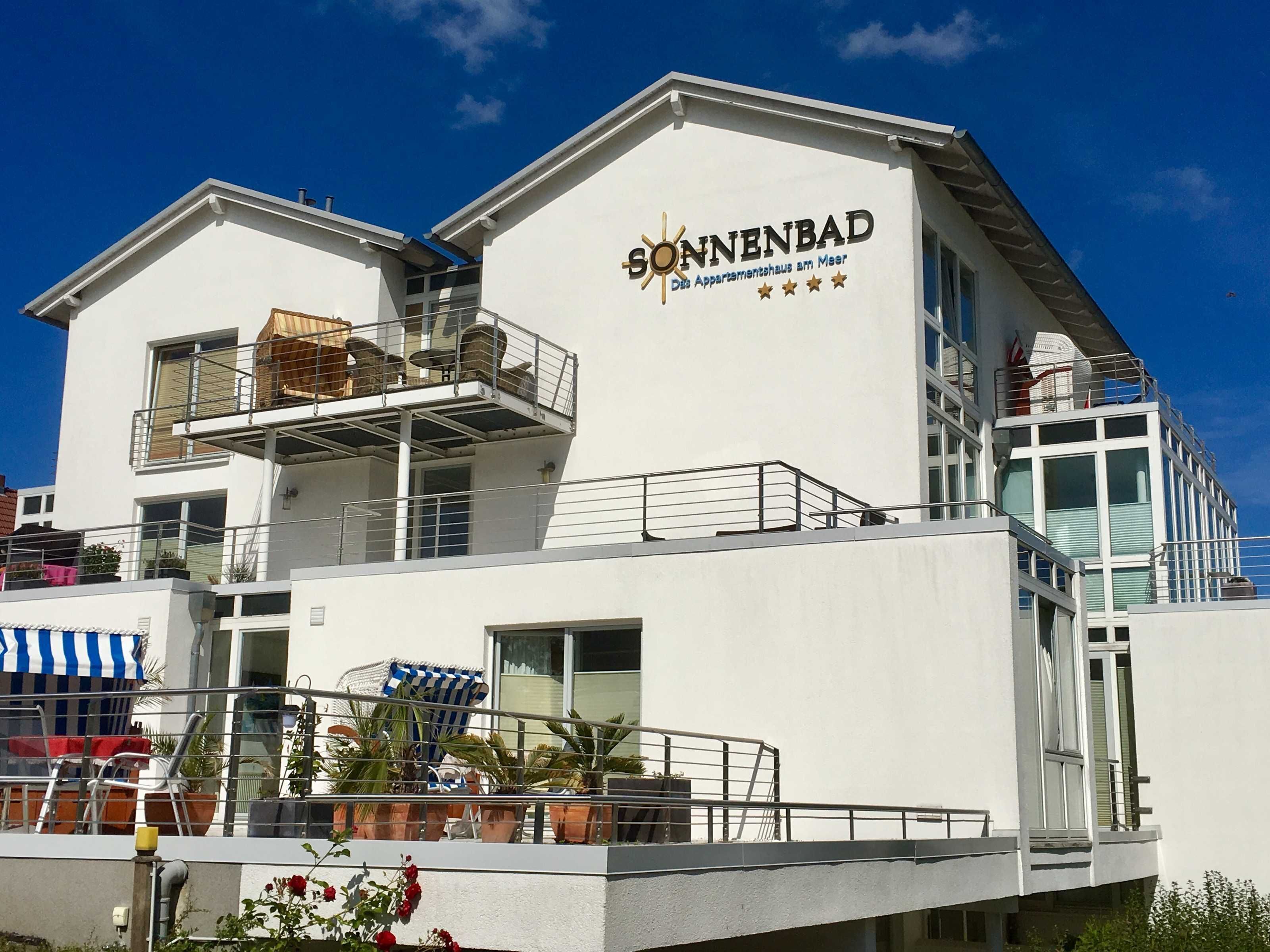 A modern building with the name 'Sonnenbad' and a sign indicating it is a hotel. There are balconies with railings and potted plants.