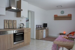 Una cocina moderna con armarios de madera, horno empotrado y cafetera. Hay un televisor sobre un mueble de madera y un reloj en la pared.