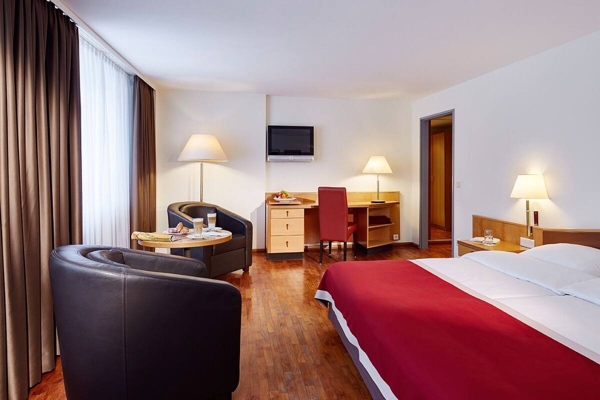 A hotel room with a bed, a desk, a chair, a TV, and a lamp.