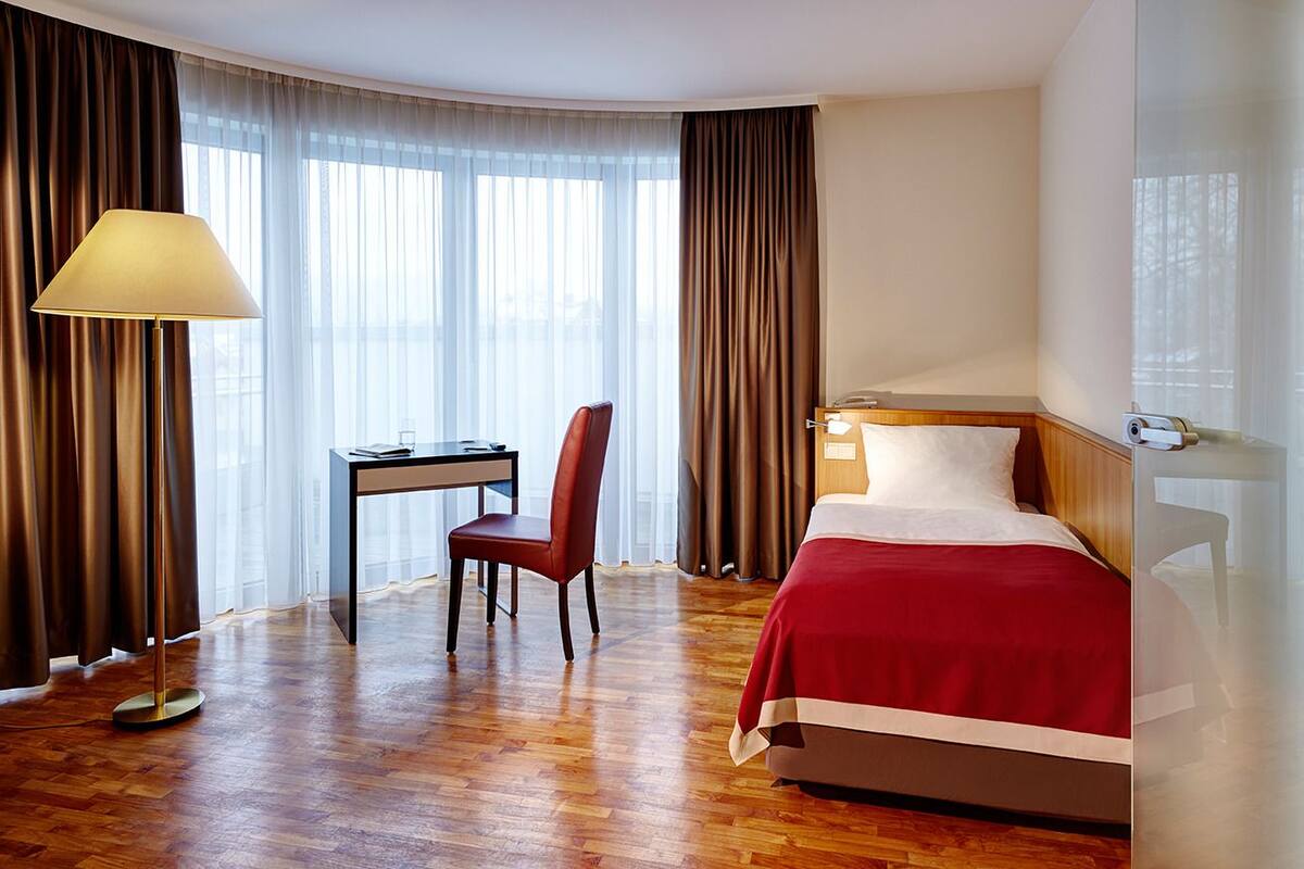 A hotel room with a bed, a desk, a chair, and a lamp.