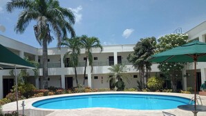 A swimming pool surrounded by a courtyard with palm trees and a multi-story building. - Hotel La Via (Cartagena)
