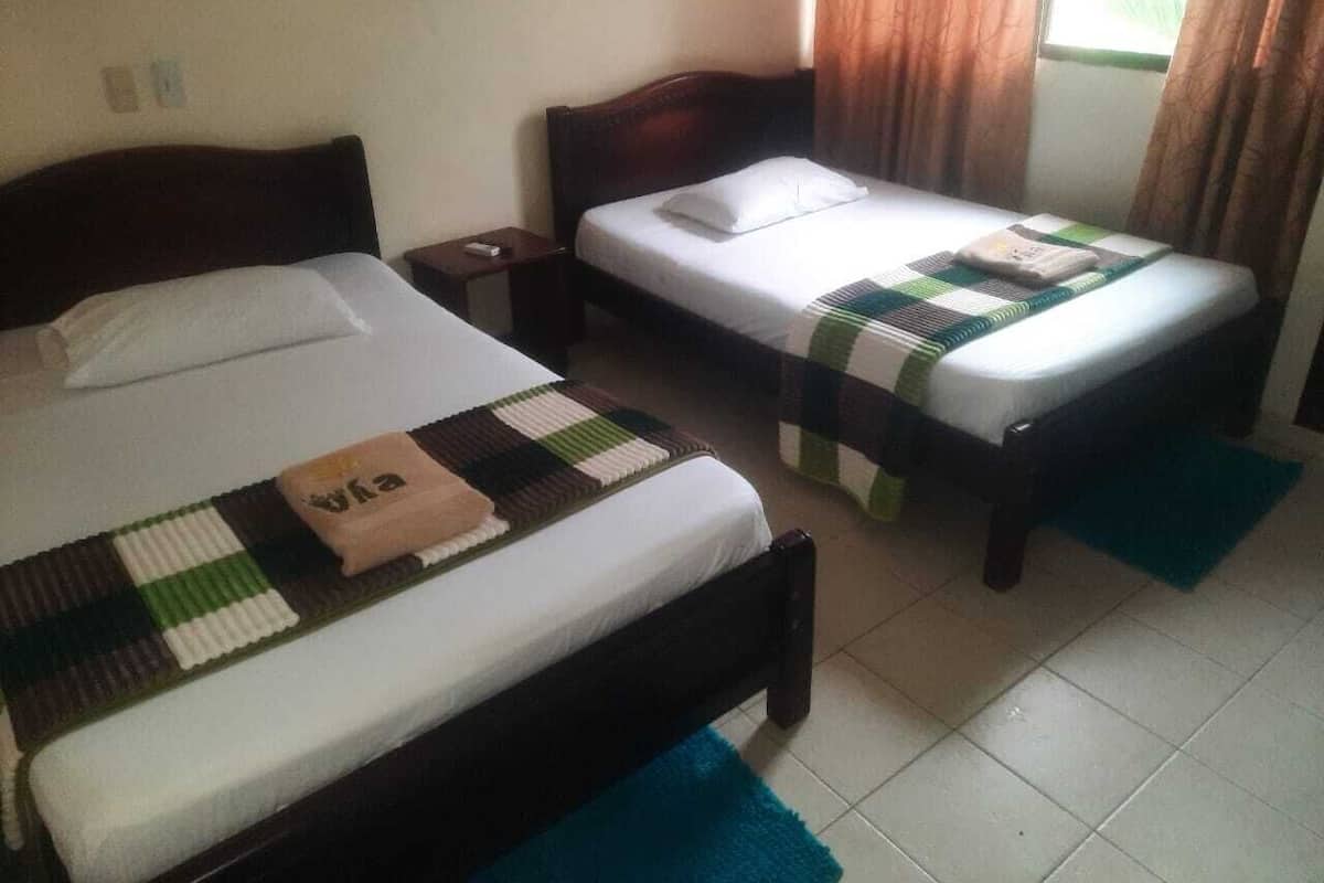 A hotel room with two single beds, a nightstand, a small table, and a window with curtains.