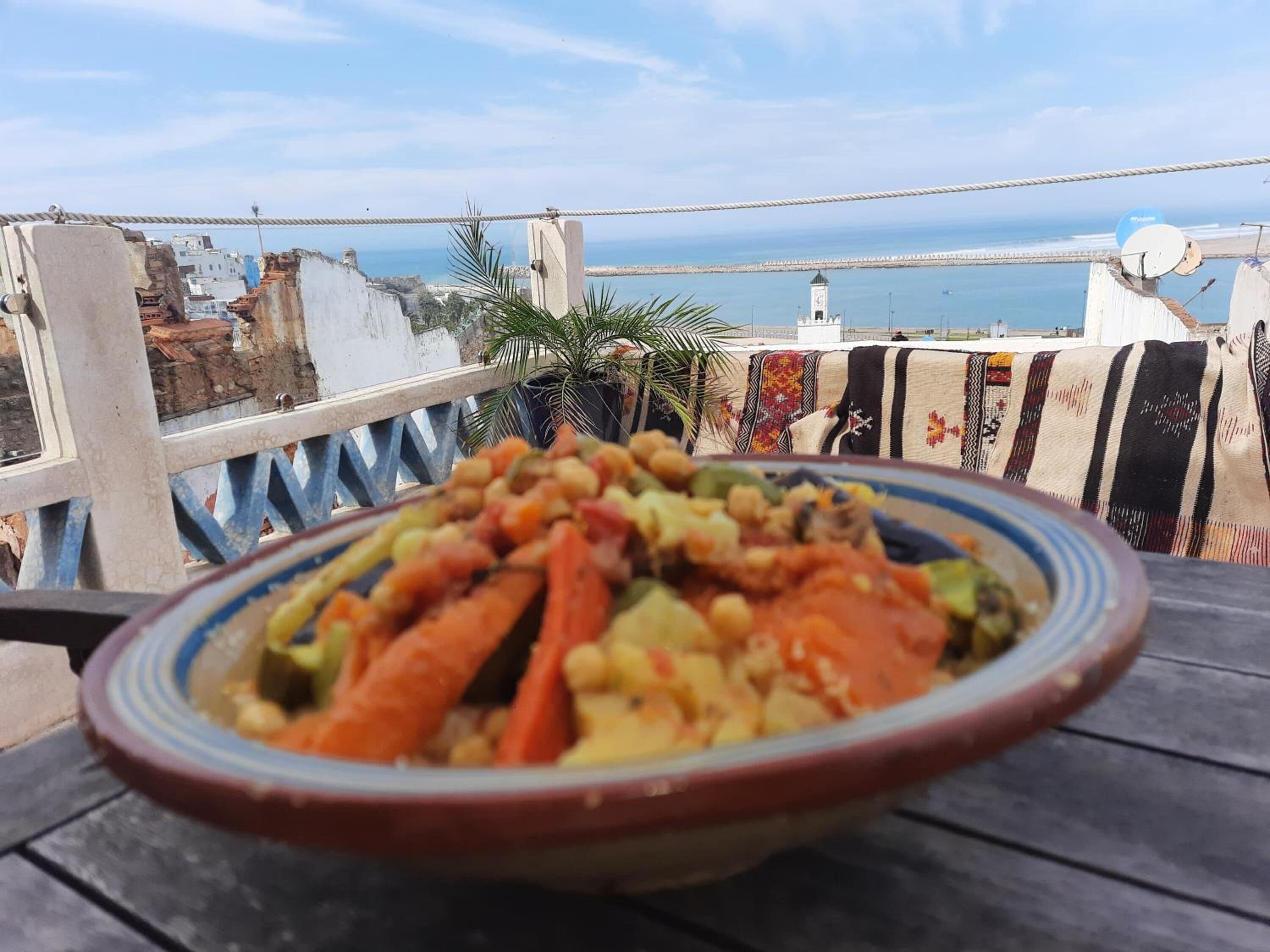 Una mesa con un cuenco de estofado de verduras, una planta en maceta y vistas al mar y edificios.
