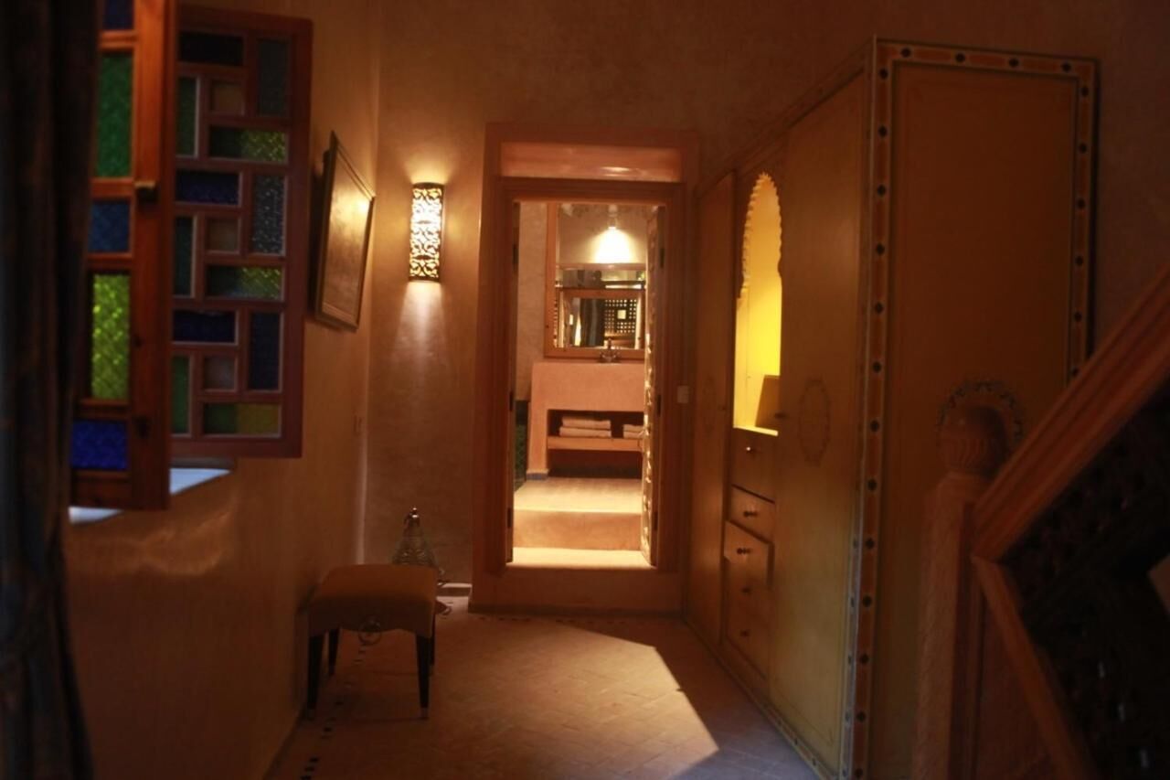 A narrow hallway with a wooden bench, a small table, and a door leading to a room with a bed.