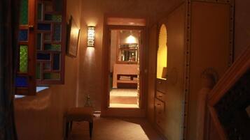 A narrow hallway with a wooden bench, a small table, and a door leading to a room with a bed.