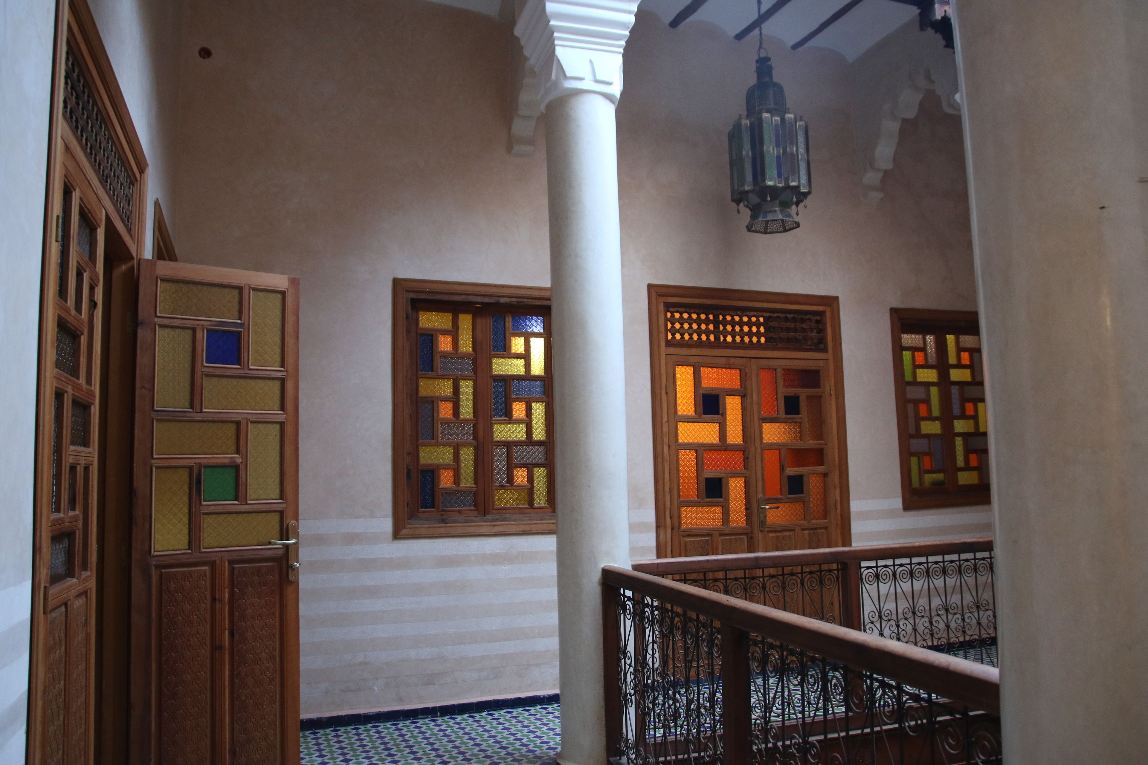 A hallway with traditional wooden doors and a patterned floor, leading to a balcony with a metal railing.