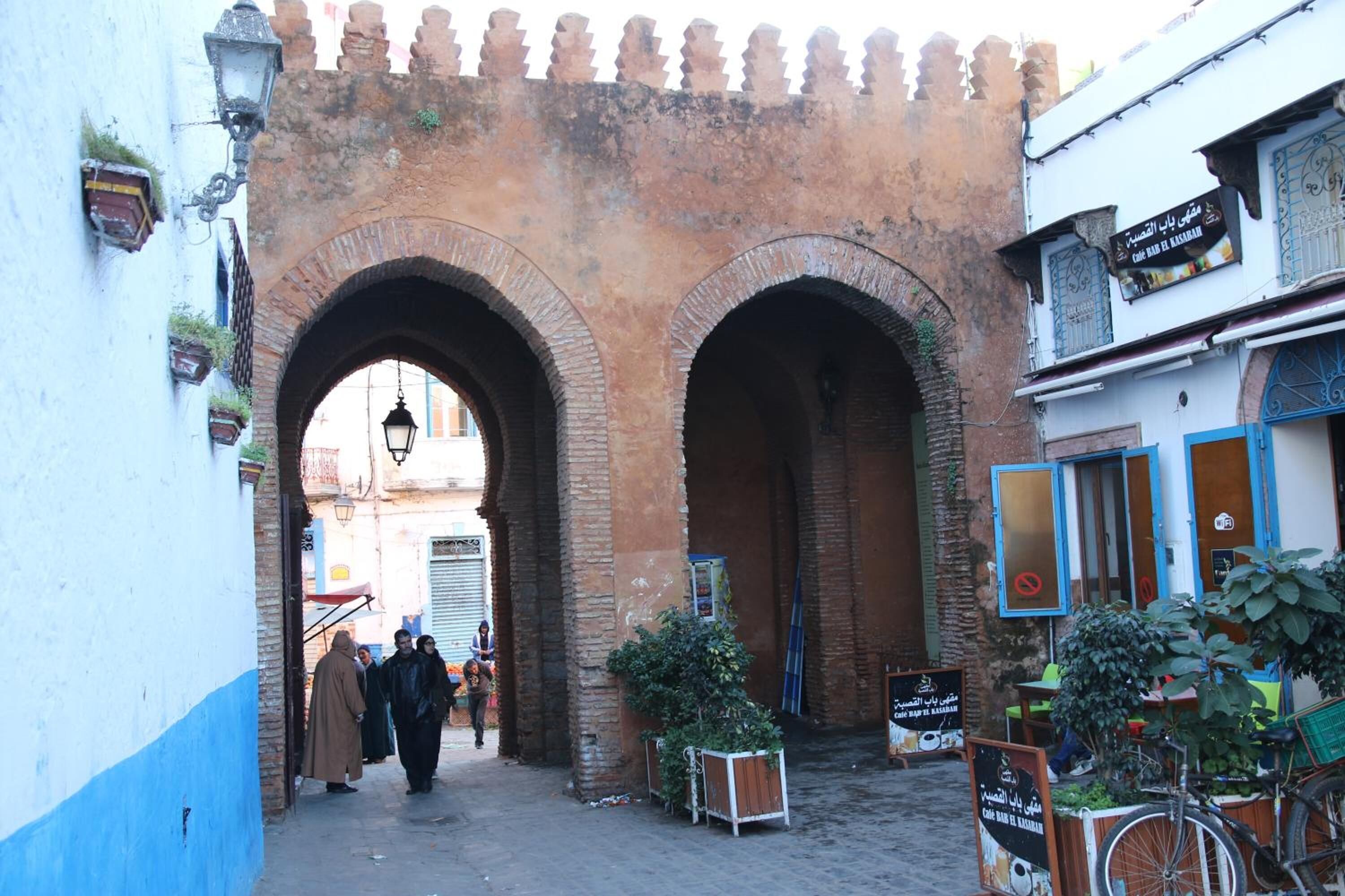 Una calle estrecha con un gran arco de ladrillo. Se ven personas caminando y una bicicleta estacionada cerca de un edificio con un letrero.