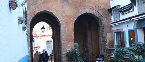 Una calle estrecha con un gran arco de ladrillo. Se ven personas caminando y una bicicleta estacionada cerca de un edificio con un letrero.