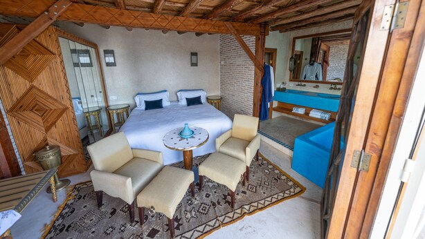 A bedroom with a bed, two chairs, a small table, and a mirror.