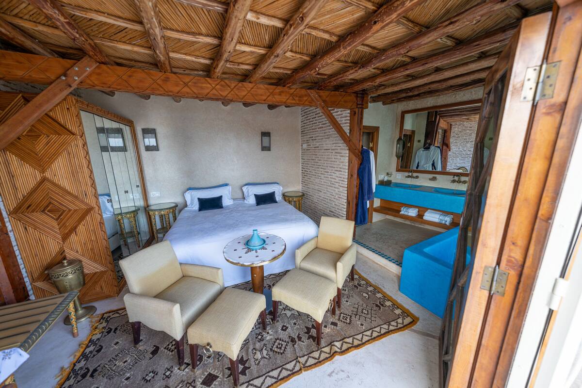 A bedroom with a bed, two chairs, a small table, and a mirror.