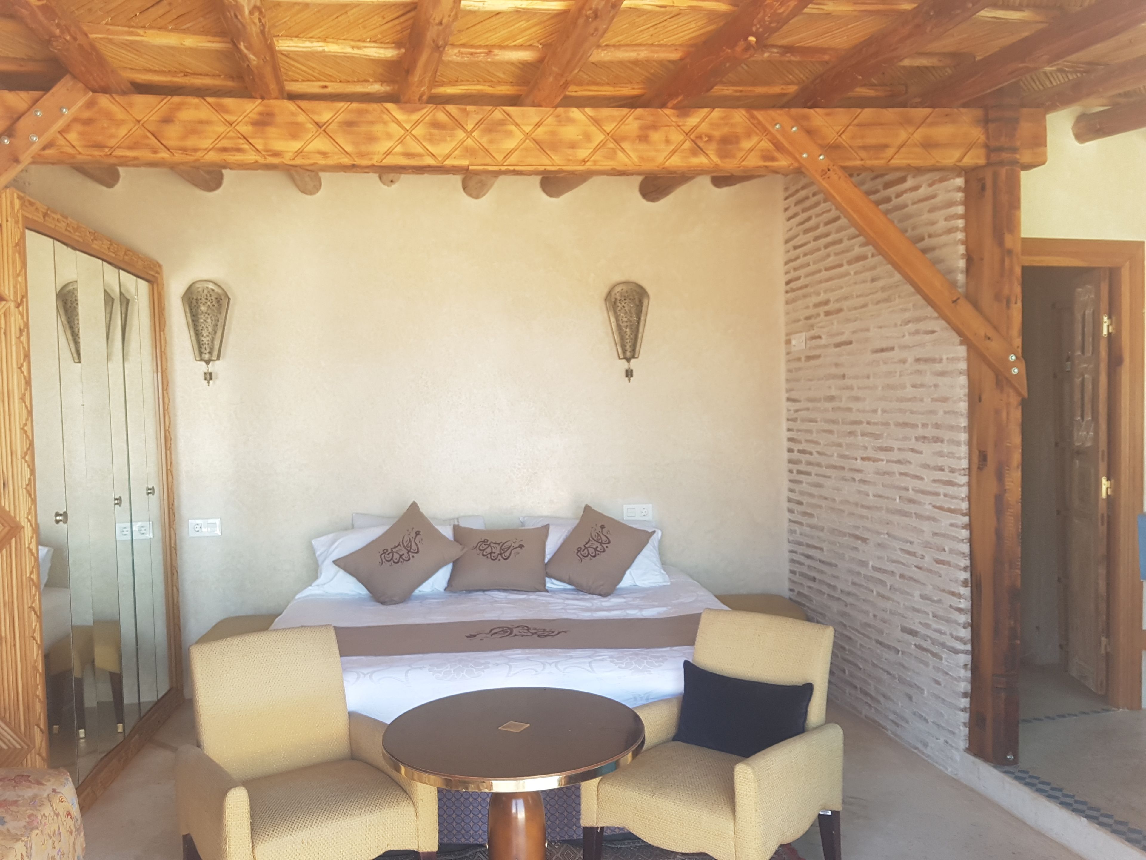 Une chambre à coucher avec un lit, deux lampes fixées au mur, un plafond en bois, un mur en briques et une porte.