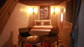 Un dormitorio acogedor con una cama, dos sillas, una mesita y un ventanal decorativo.