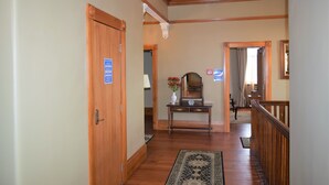 Un couloir avec un plancher en bois, une porte en bois, une console sur laquelle est posé un vase de fleurs et un miroir.
