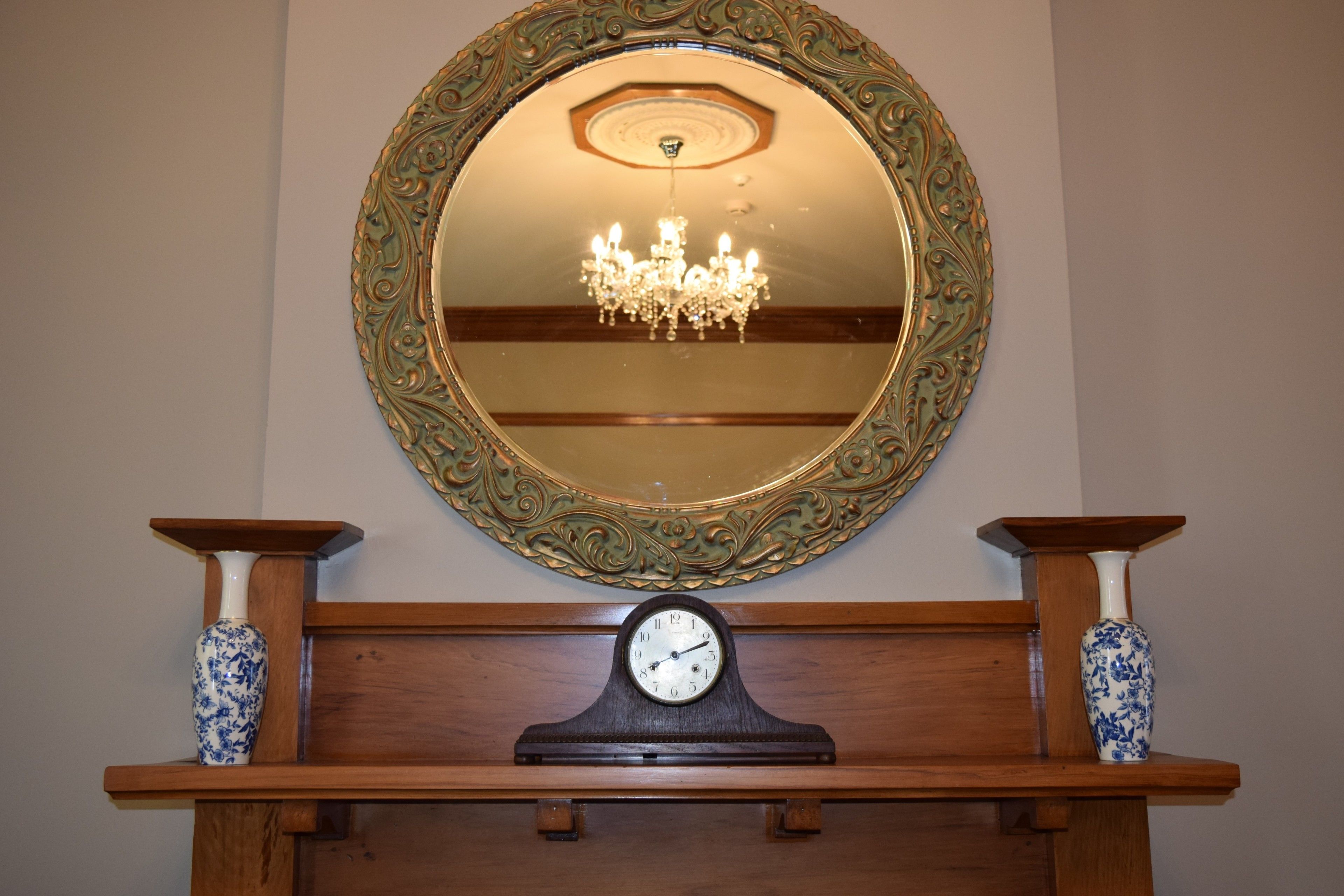 Un miroir avec un cadre orné, une horloge en dessous et deux vases de chaque côté.