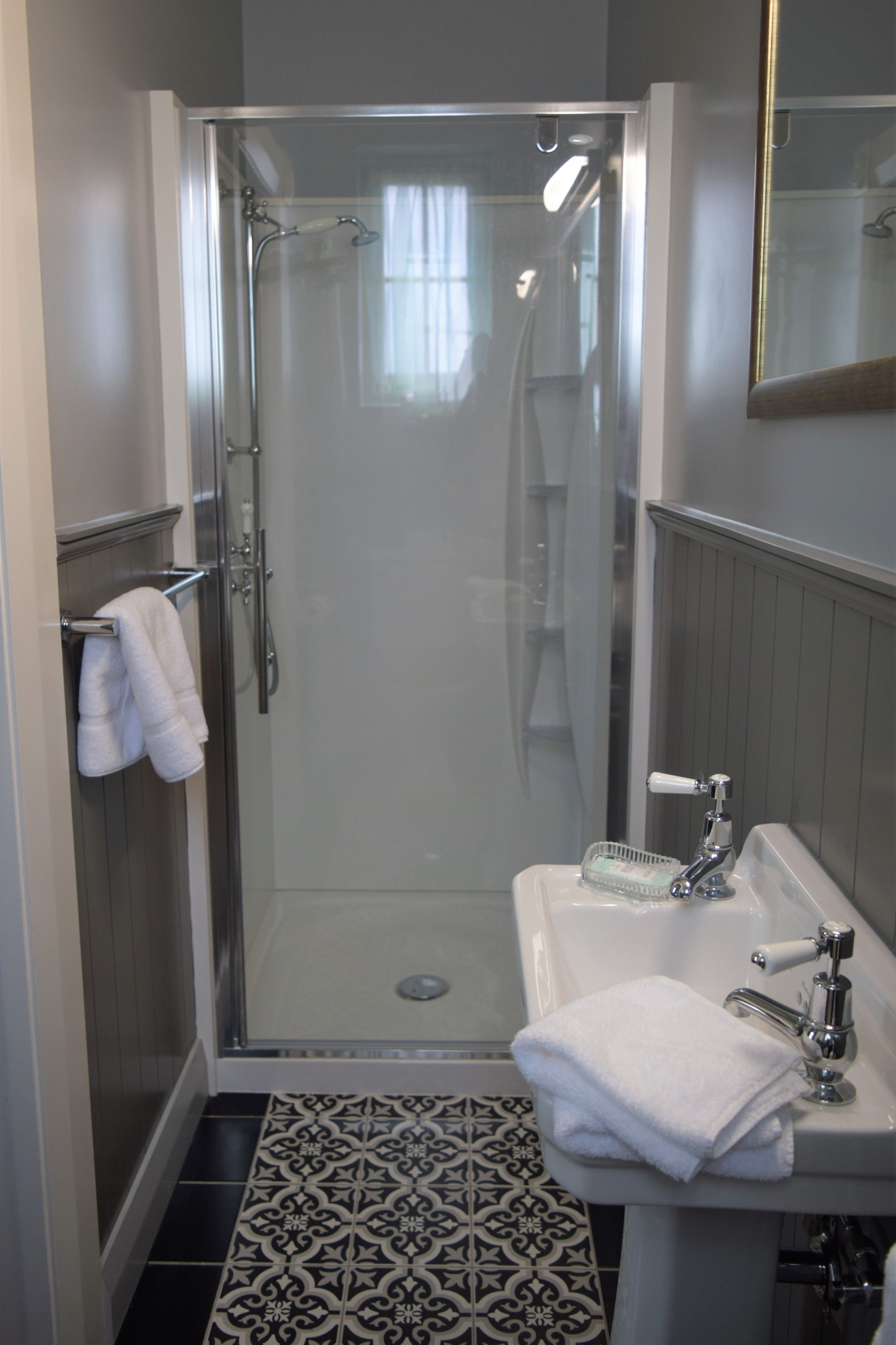 A modern bathroom with a glass-enclosed shower, a white sink with a mirror, and a patterned floor.
