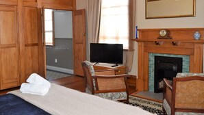 Une chambre d’hôtel avec un lit, deux fauteuils en osier, une télévision, une cheminée et des armoires en bois.