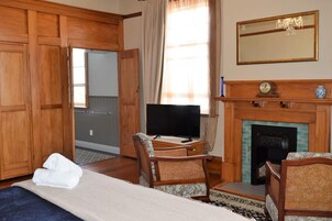 Una habitación de hotel con una cama, dos sillones de mimbre, un televisor, una chimenea y armarios de madera.