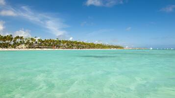 A beach with clear turquoise water, palm trees, and a resort area in the background.