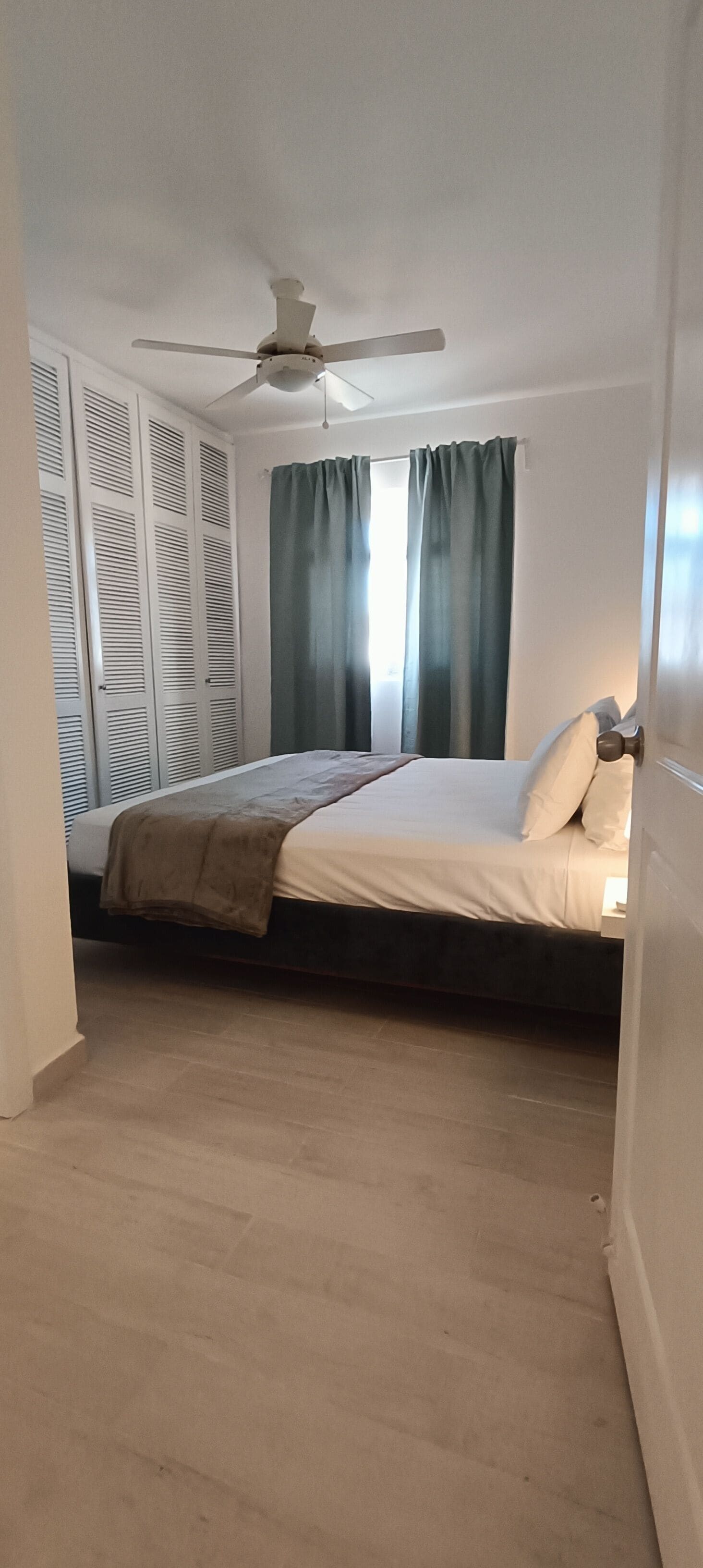 A bedroom with a bed, a ceiling fan, and a window with curtains.